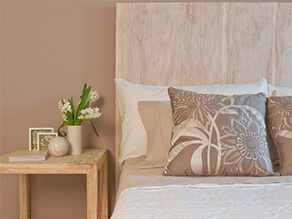 Neutral brown bedroom featuring wooden bedhead and side table with green plant and cushions
